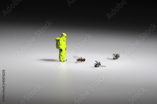 tiny firefighter figure in hazmat suit stands next to dead flies