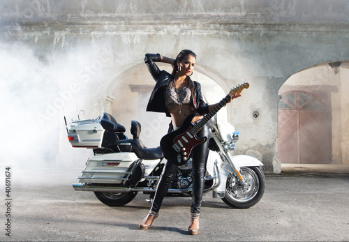 A young Caucasian woman with a guitar posing near a bike