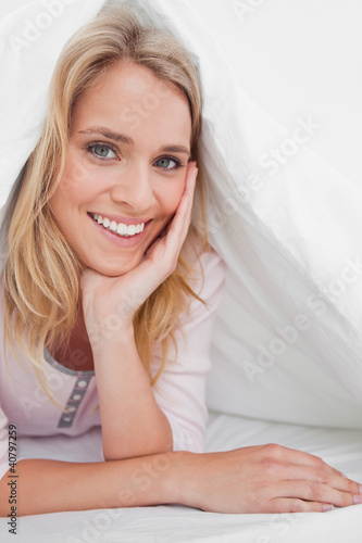 Close up  woman under the quilt smiling with her hand supporting