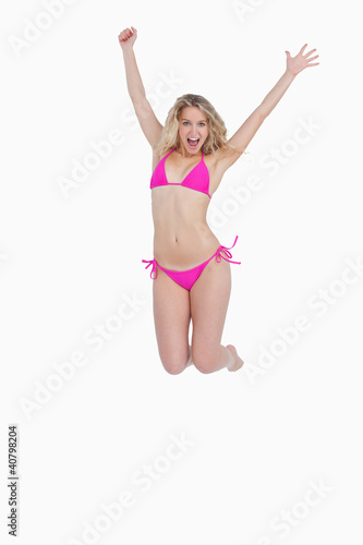 Dynamic blonde woman energetically jumping while wearing swimsui