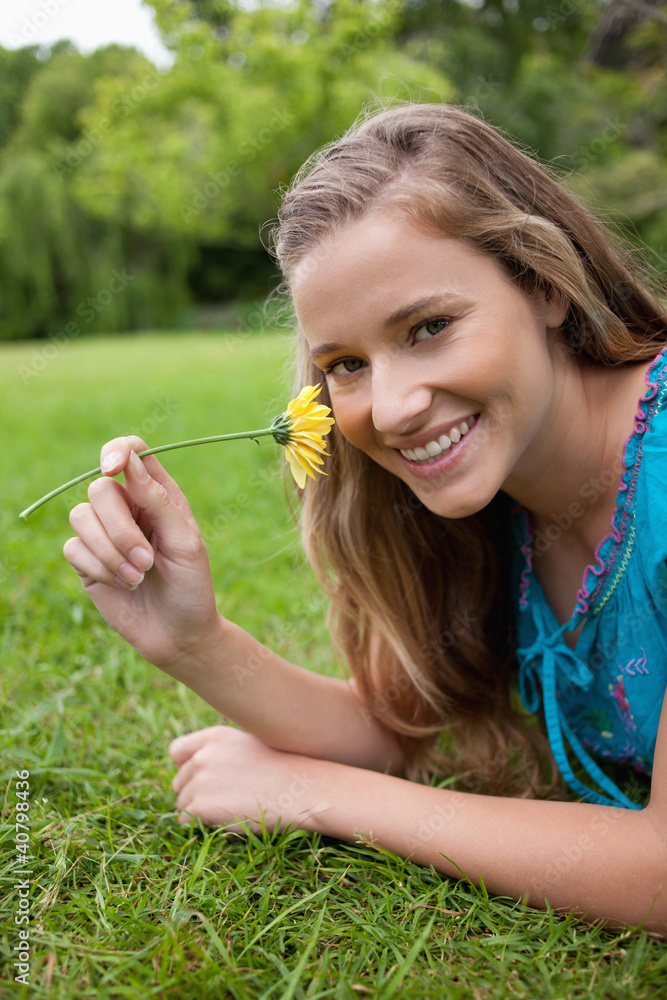 Young smiling girl smelling a yellow flower while lying on the g Young smiling girl smelling a yellow flower while lying on the g