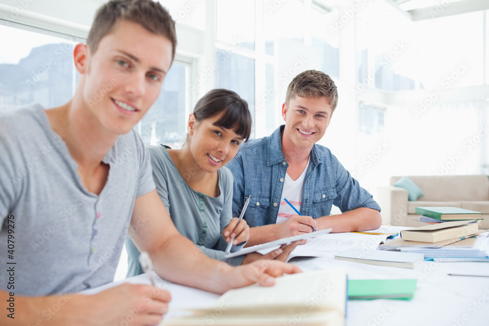 Three students sitting together as they all look into the camera Three students sitting together as they all look into the camera