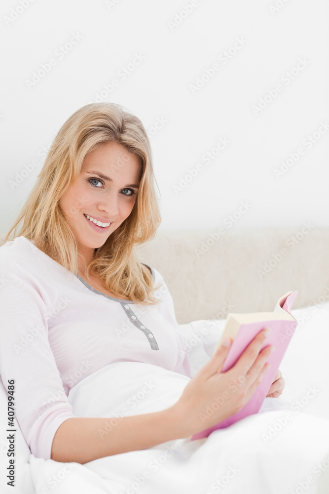 Woman in bed holding her book, looking sideways slightly and smi Woman in bed holding her book, looking sideways slightly and smi