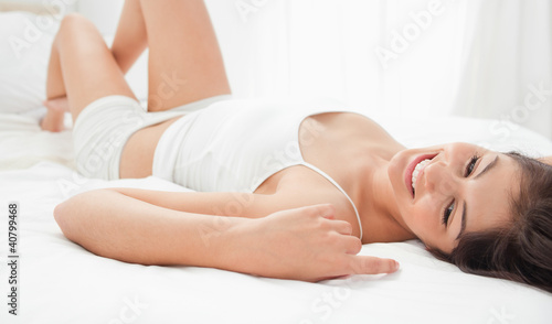 Woman relaxing on her bed on her back, smiling with a knee raise