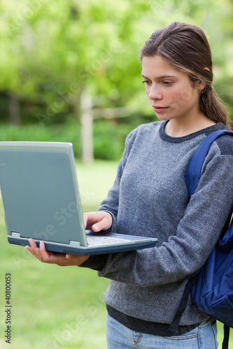 Serious student typing on her laptop while standing upright in a