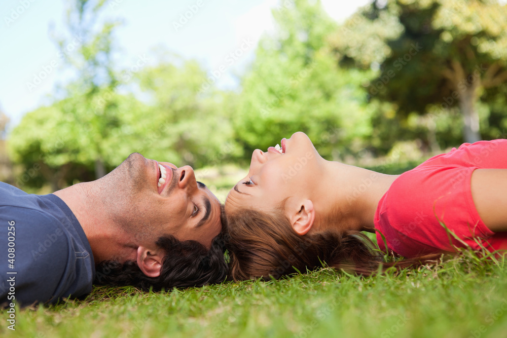 Two smiling friends looking at each other while lying head to he Two smiling friends looking at each other while lying head to he