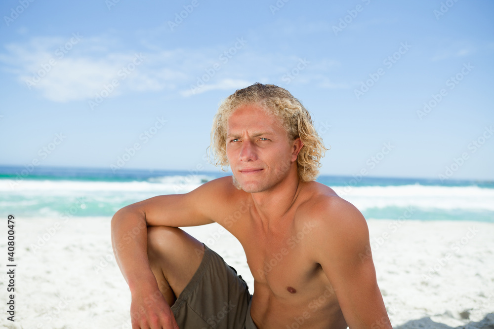 Serious man sitting on the beach while looking towards the side Serious man sitting on the beach while looking towards the side