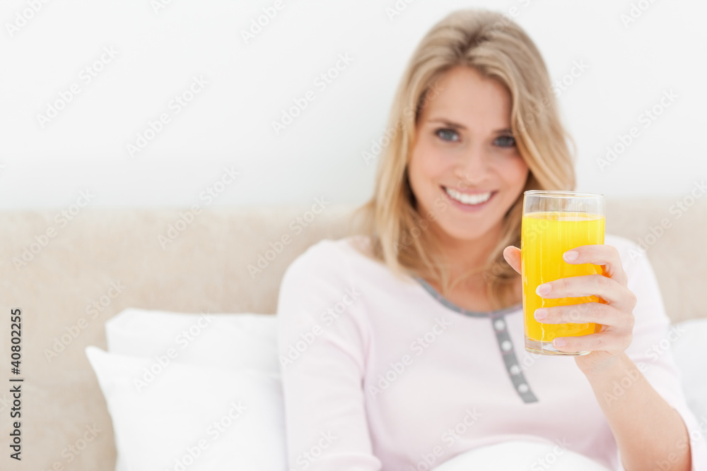 Woman holding a glass of orange juice while smiling and looking Woman holding a glass of orange juice while smiling and looking