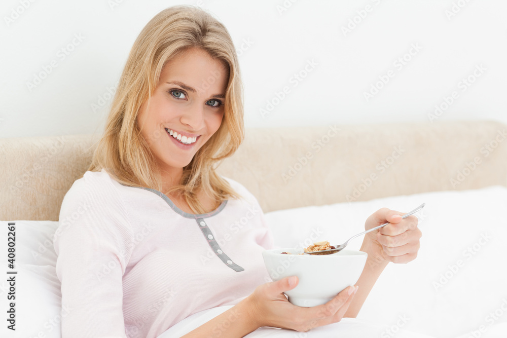 Woman in bed with a bowl of cereal in hand and a slightly raised Woman in bed with a bowl of cereal in hand and a slightly raised