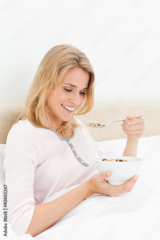 Woman in bed with a bowl of cereal, looking down at the spoon by Woman in bed with a bowl of cereal, looking down at the spoon by