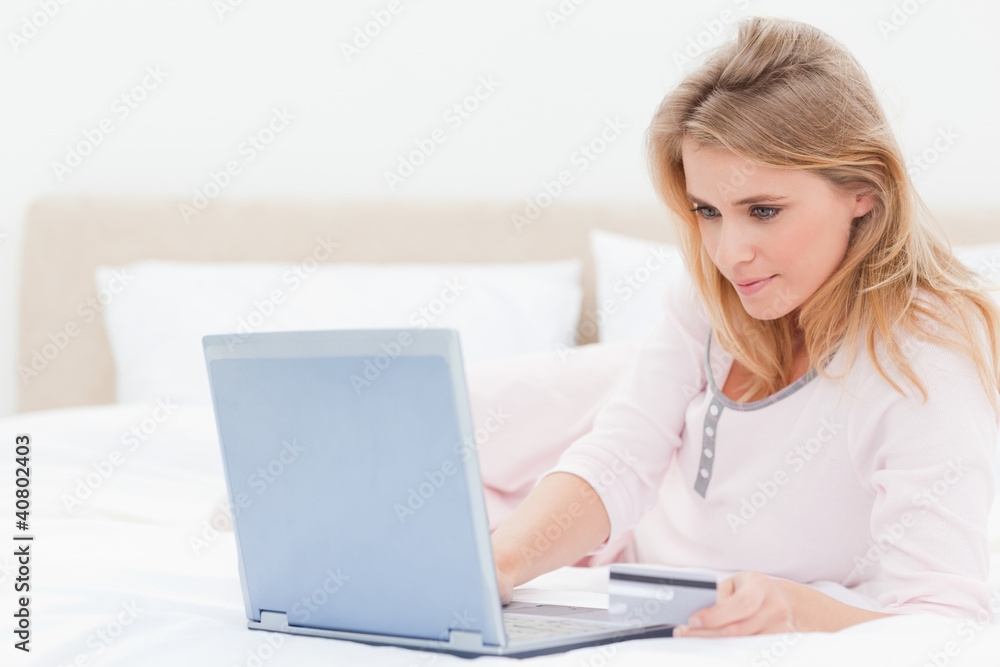 Woman lying on a bed with her laptop, looking at the screen Woman lying on a bed with her laptop, looking at the screen