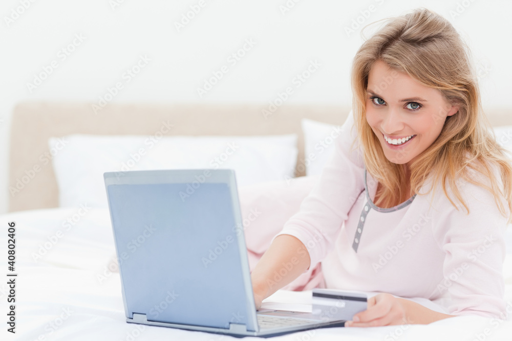 Woman lying on the bed, with a laptop in hand and looking forwar Woman lying on the bed, with a laptop in hand and looking forwar