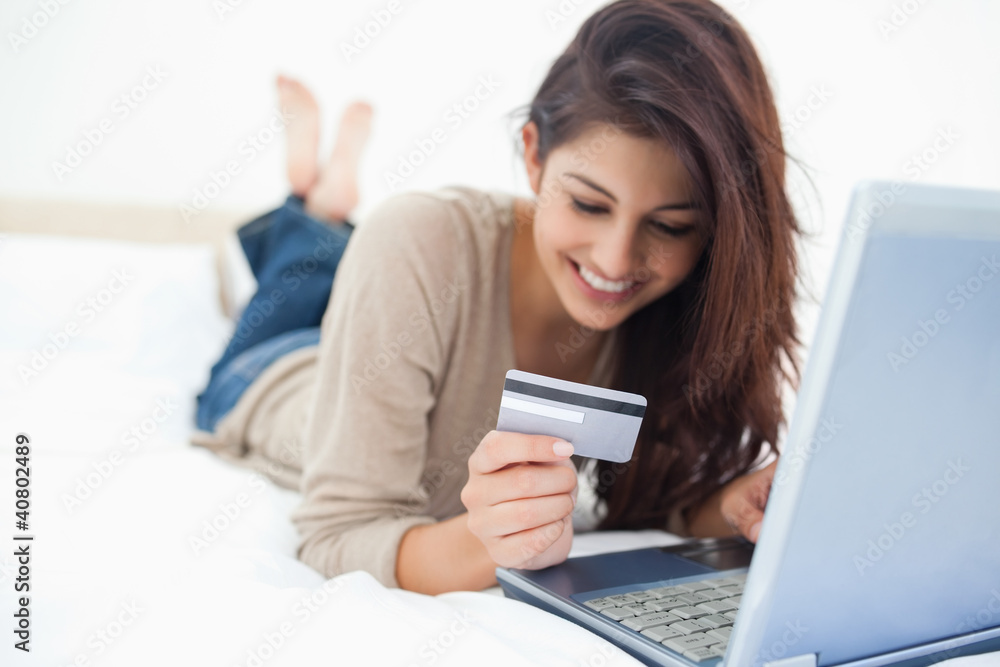 Smiling woman on her laptop reading her credit card details on t Smiling woman on her laptop reading her credit card details on t