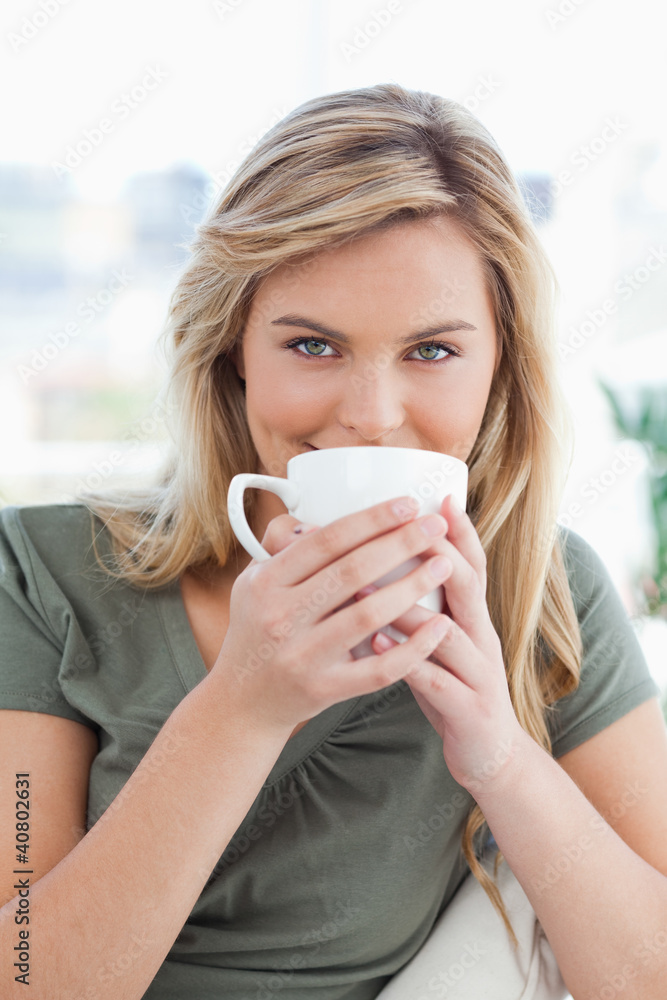 Close up, woman with a mug held up in front of her mouth and loo Close up, woman with a mug held up in front of her mouth and loo