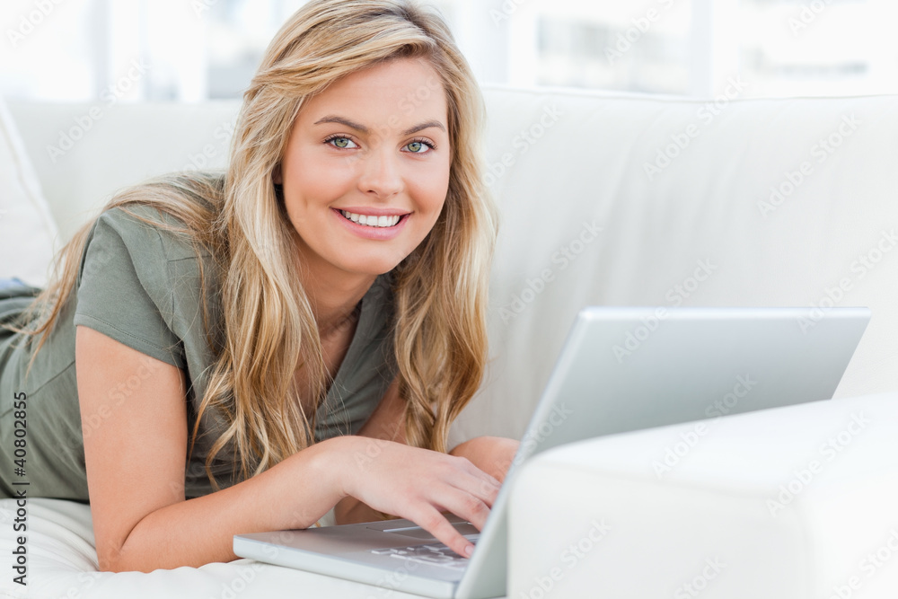 Woman lying across the couch, smiling as she looks forward, usin Woman lying across the couch, smiling as she looks forward, usin