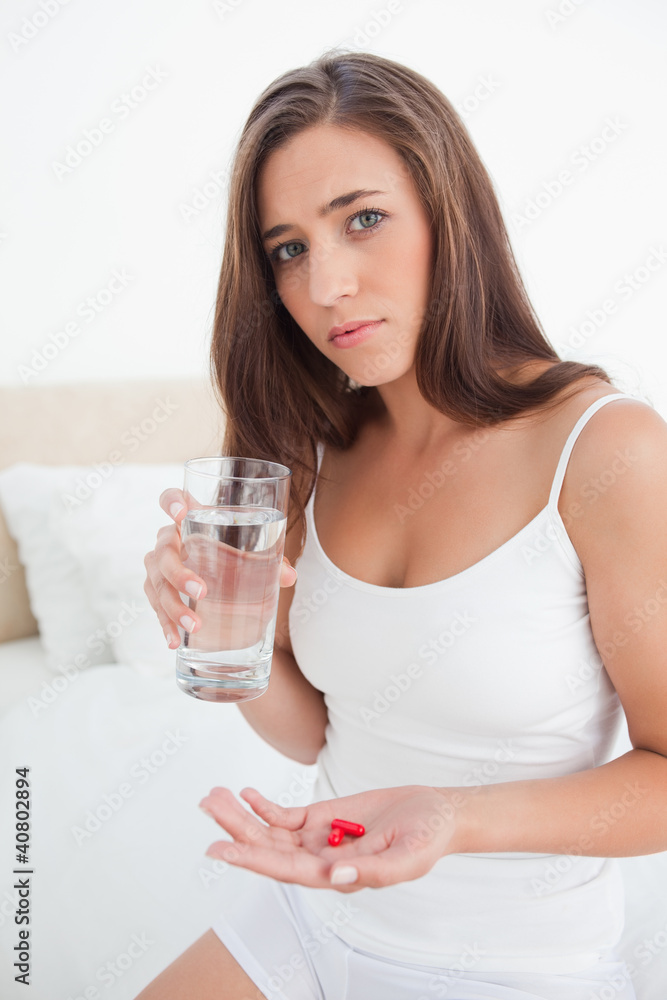 Woman looking worried as she is about to take two pills with wat Woman looking worried as she is about to take two pills with wat