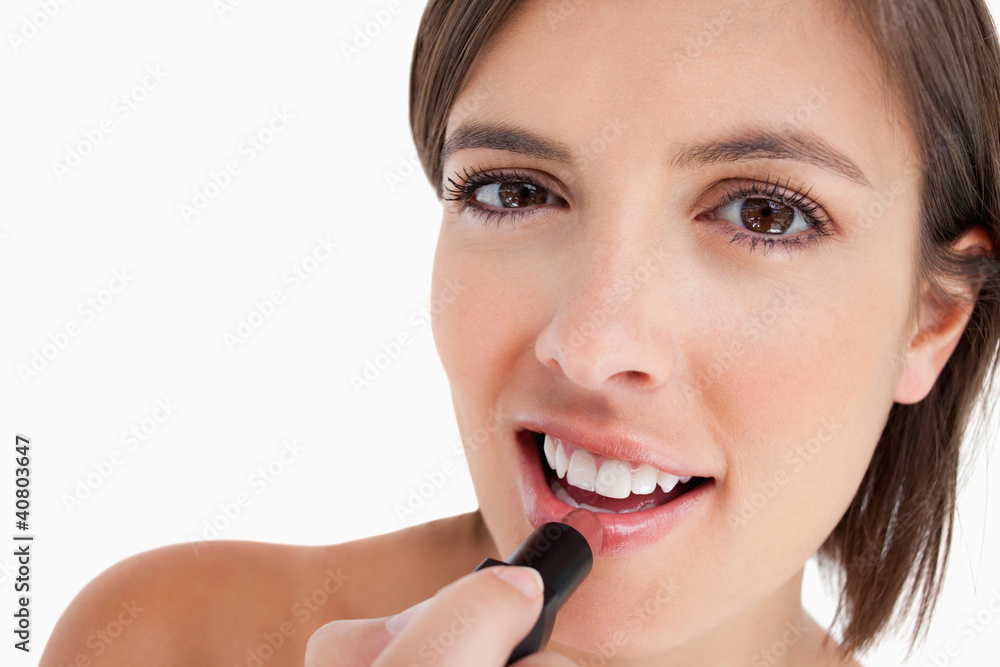 Smiling teenage girl applying make-up while putting on lipstick