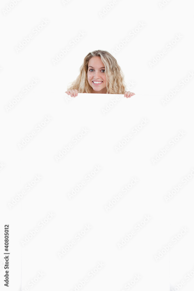 Smiling young woman hiding her body behind a blank poster Smiling young woman hiding her body behind a blank poster