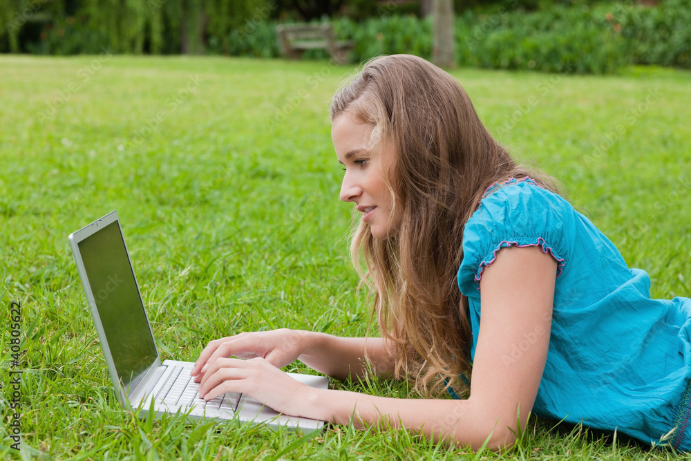 Side view of a young girl typing on her laptop while lying down Side view of a young girl typing on her laptop while lying down