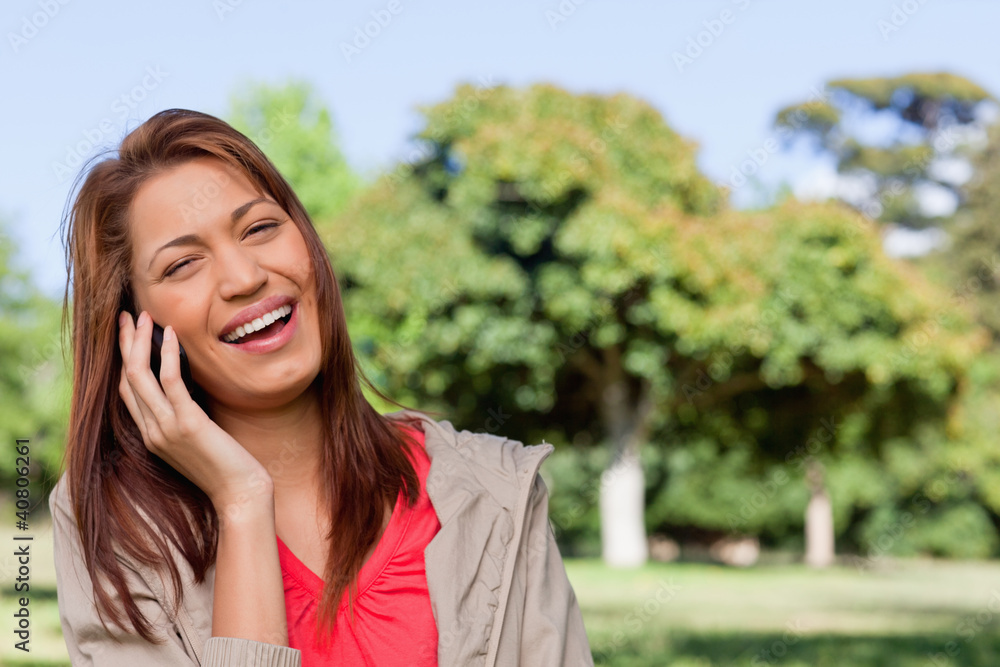 Young woman laughing happily on the phone in a bright park area