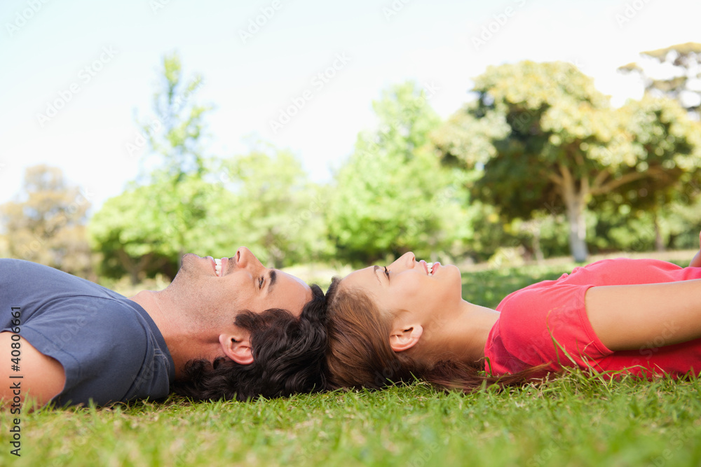 Two smiling friends looking upwards while lying head to head Two smiling friends looking upwards while lying head to head