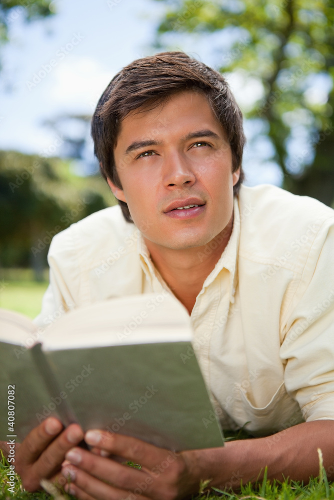 Man looks to the distance while reading a book as he is lying do Man looks to the distance while reading a book as he is lying do