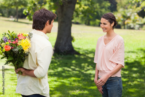 Woman smiling as her friend approaches her with flowers