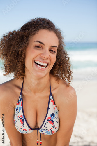 Young woman laughing while standing on the beach and leaning her