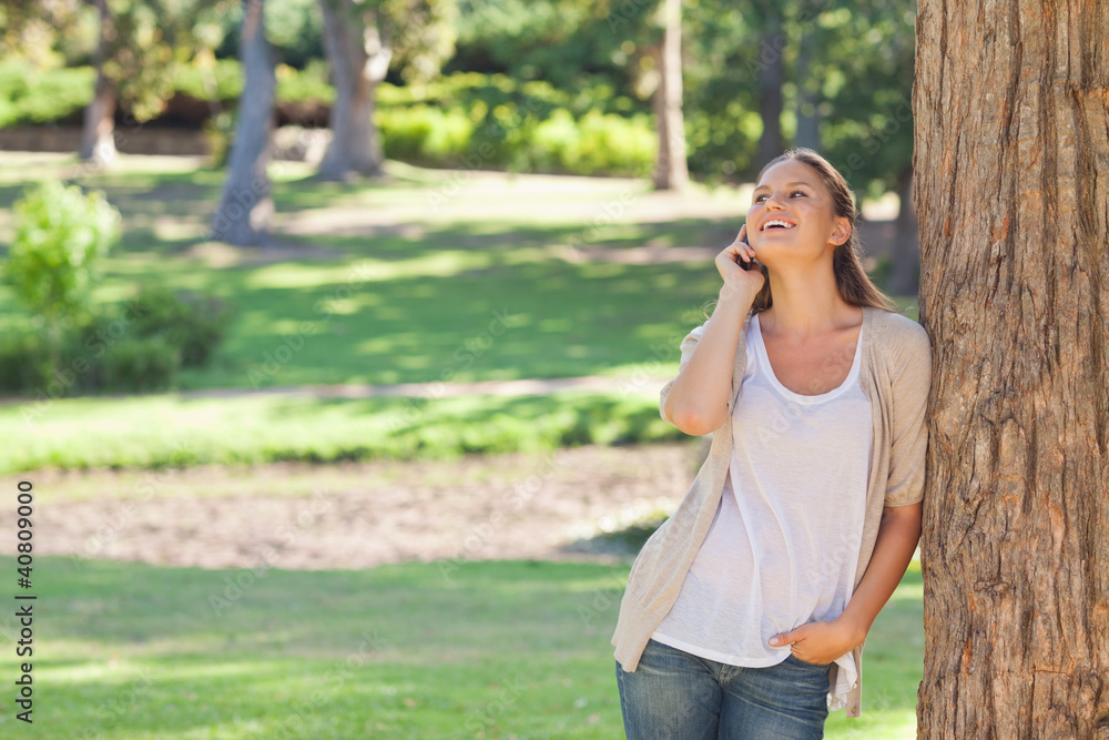 Cheerful woman on the phone leaning against a tree Cheerful woman on the phone leaning against a tree