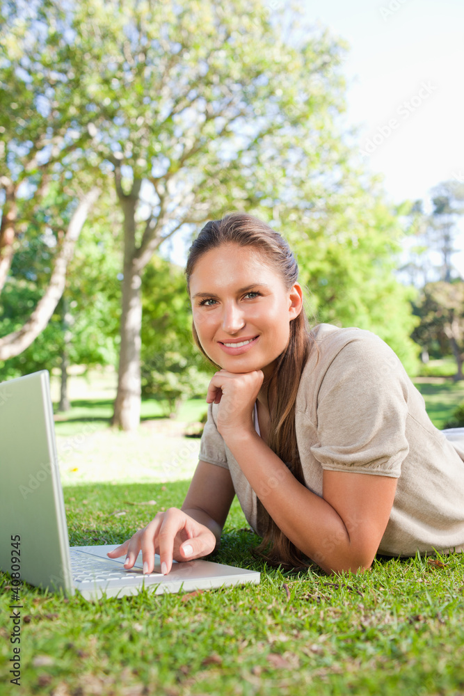 Smiling woman with her laptop while lying on the lawn Smiling woman with her laptop while lying on the lawn