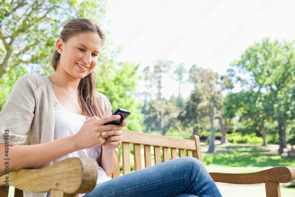 Smiling woman reading text message on a park bench Smiling woman reading text message on a park bench