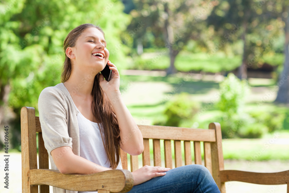 Laughing woman on her cellphone on a park bench Laughing woman on her cellphone on a park bench