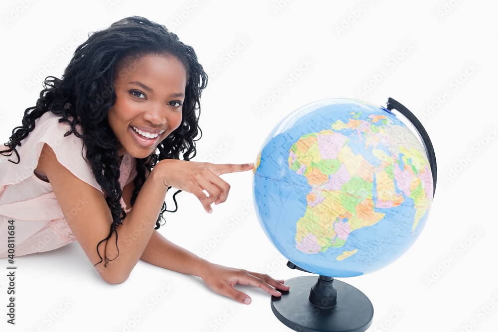 Fototapeta premium A young girl smiling at the camera has her finger on a globe
