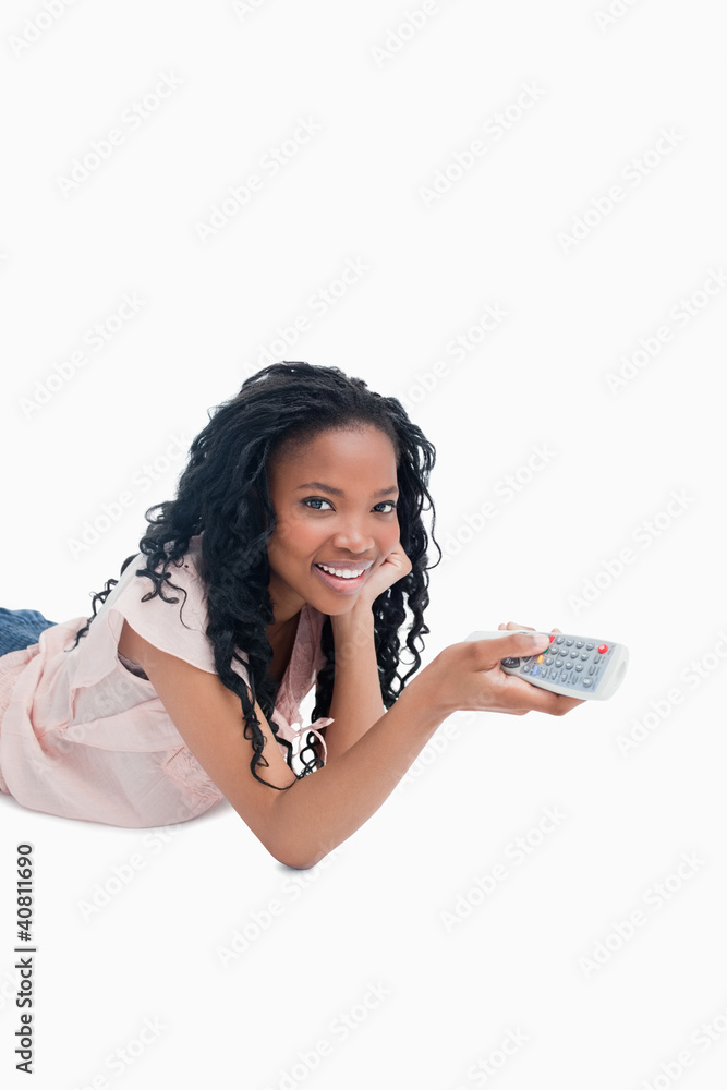A young girl holding a television remote control is smiling at t A young girl holding a television remote control is smiling at t