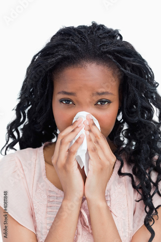 A young woman is blowing her nose in a tissue