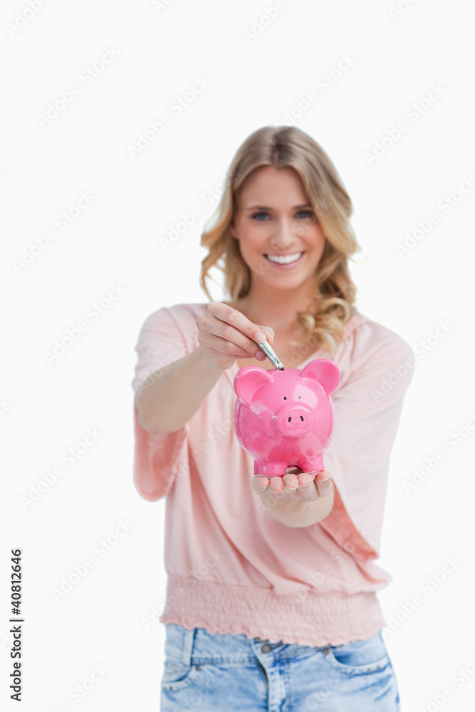 Woman holding a piggy bank is putting money into it Woman holding a piggy bank is putting money into it