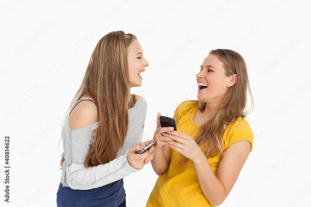 Two young women laughing while holding their cellphones Two young women laughing while holding their cellphones