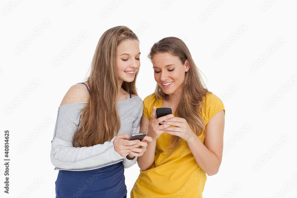 Two young women smiling while looking their cellphones Two young women smiling while looking their cellphones