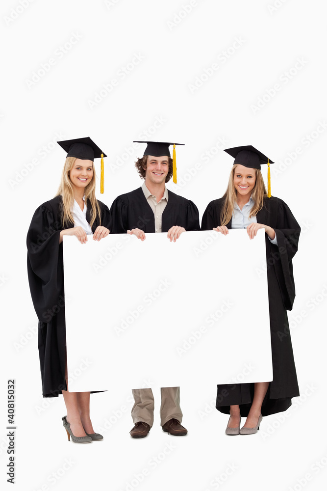 Three students in graduate robe holding a blank sign Three students in graduate robe holding a blank sign