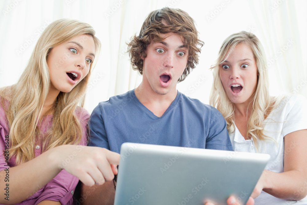 Three shocked friends looking at the screen of the tablet Three shocked friends looking at the screen of the tablet