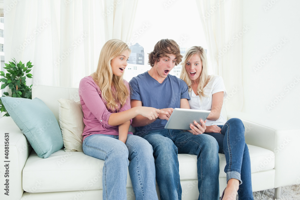 Three friends looking at the screen of the tablet in shock and p Three friends looking at the screen of the tablet in shock and p