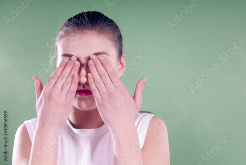 Beautiful young woman with eyse closed by hands in studio photo