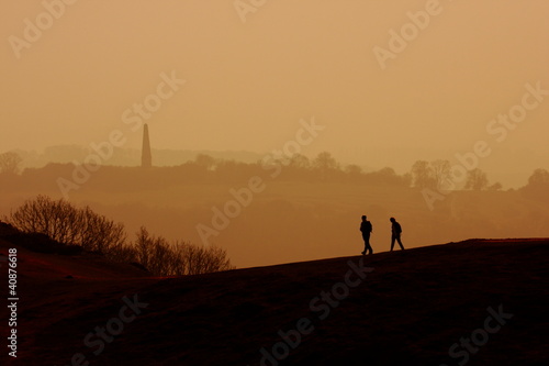 Two people walking along a hilltop in the afternoon sun