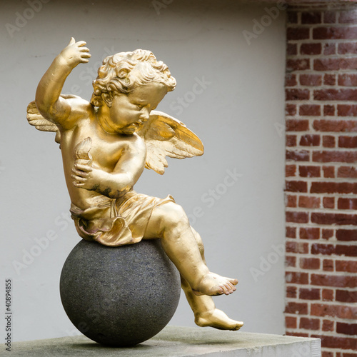 A golden putto sitting on a round stone