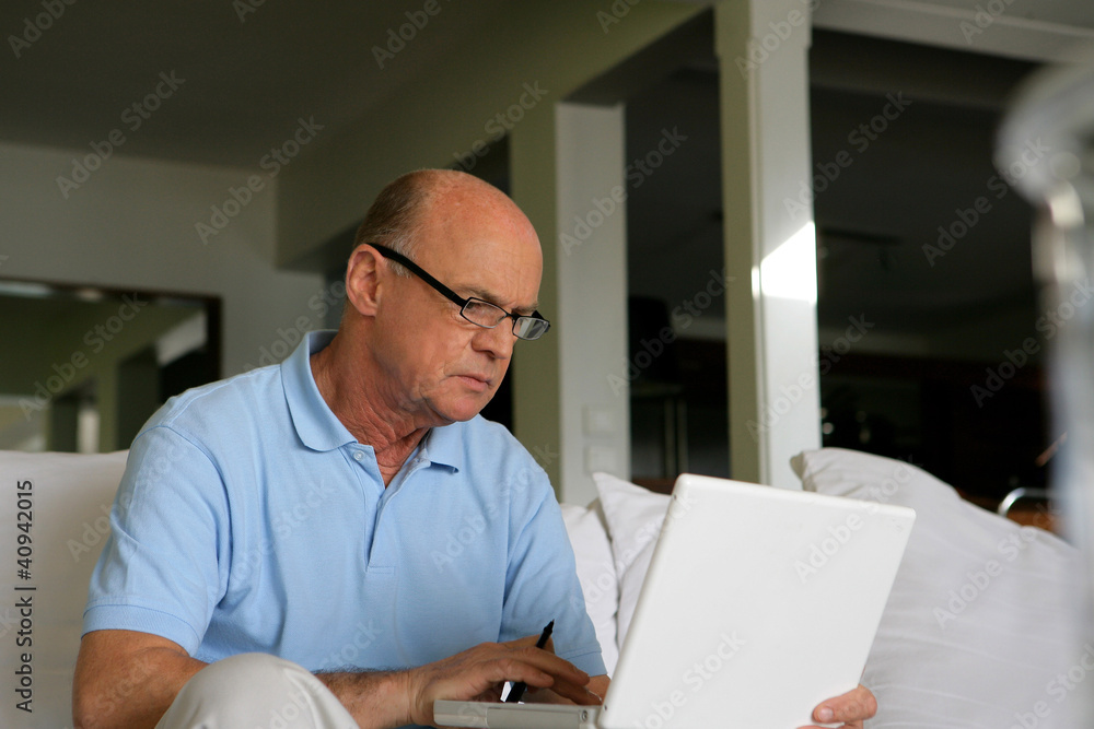 Senior man sitting on a sofa in front of a laptop computer Senior man sitting on a sofa in front of a laptop computer