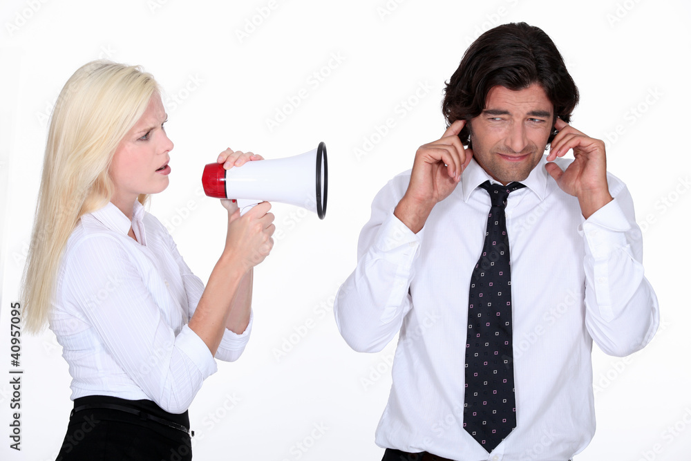 woman talking through a megaphone and a man plugging his ears woman talking through a megaphone and a man plugging his ears