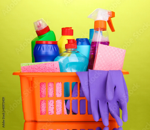 Basket with cleaning items on green background