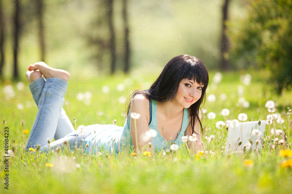 Cute woman with white laptop in the park with dandelions Cute woman with white laptop in the park with dandelions