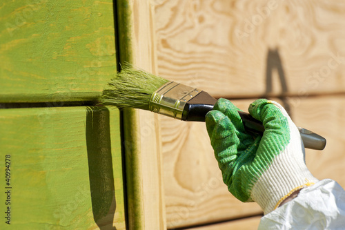 hand with a paint brush painting wooden wall in green