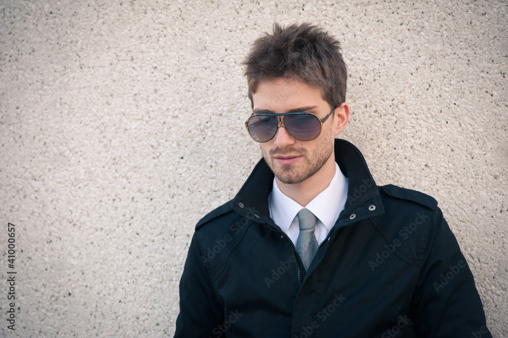 Young elegant man portrait with sunglasses against a wall. Young elegant man portrait with sunglasses against a wall.